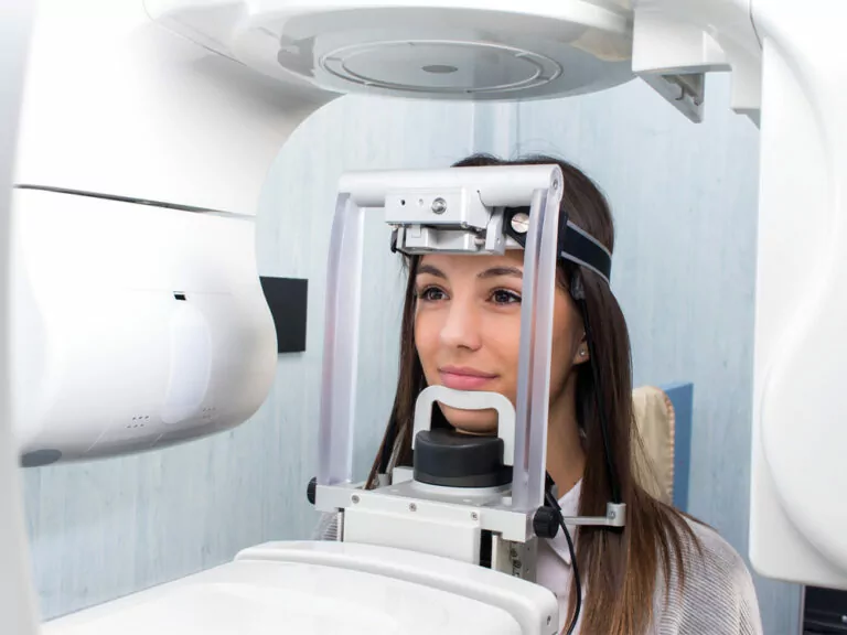 Person undergoing a dental imaging procedure using a panoramic X-ray machine, head stabilized by a headrest and chin support.